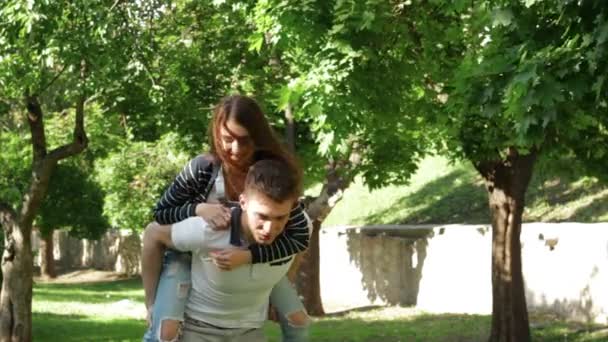 Boldog pár szórakozik a parkban és a kezében a srác a lány visel — Stock videók