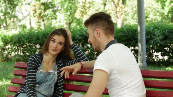 Junges schönes verliebtes Paar plaudert auf einer Bank im Park — Stockvideo