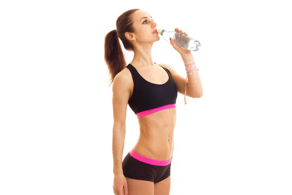 Smal ung tjej står i studion på sport topp och shorts och dricksvatten — Stockfoto