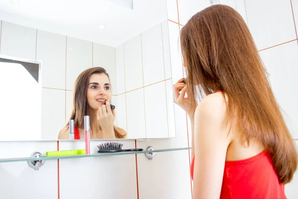Gadis cantik berambut coklat berdiri di depan cermin dan mengecat bibir — Stok Foto