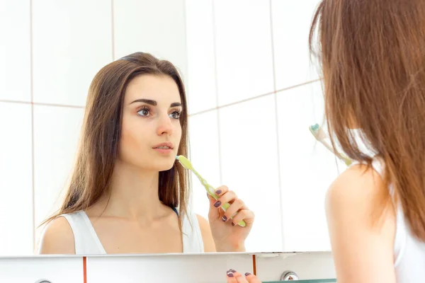 Очаровательная брюнетка подросток смотрит в зеркало и держит зубную щетку — стоковое фото
