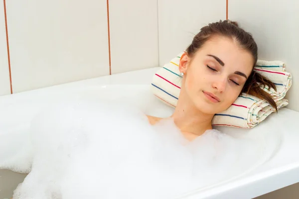 Retrato de uma jovem morena com os olhos fechados que fica em uma banheira de hidromassagem com espuma — Fotografia de Stock