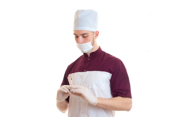 Genç bir doktor bir şapka ve bir şırınga tutarak onun yüzünde maske ile beyaz bir arka plan üzerinde izole — Stok fotoğraf