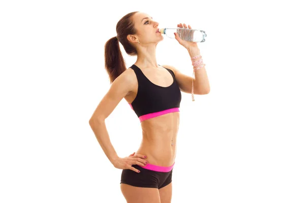 Slim fitness girl stands sideways in the Studio and drinking water from a bottle — Stock Photo, Image