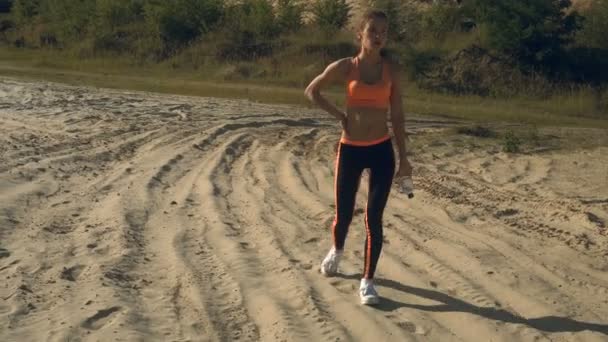 Mujer deportiva después del entrenamiento camina con agua en botella en sus manos — Vídeo de stock