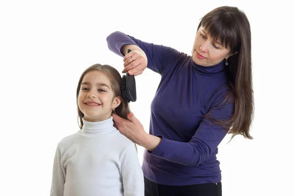 Mujer peluquero hace un peinado una niña sonriendo — Foto de Stock