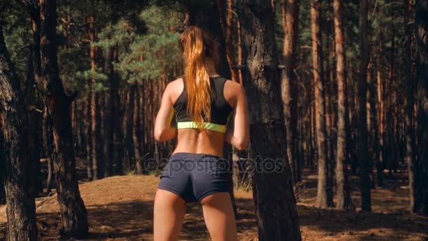 Jong meisje met sexy billen staat in de buurt van een boom in het bos en het schommelen van de macht — Stockvideo