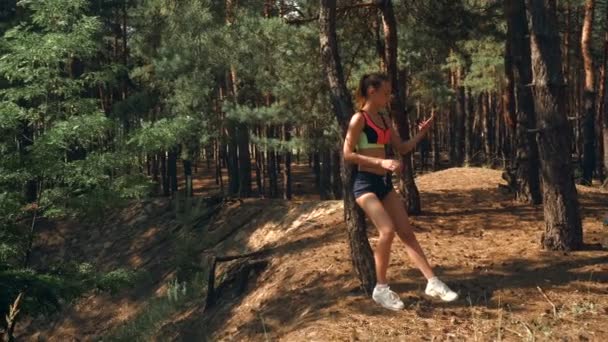 Menina bonita atlética em shorts curtos e top fica perto de uma árvore e faz uma foto — Vídeo de Stock