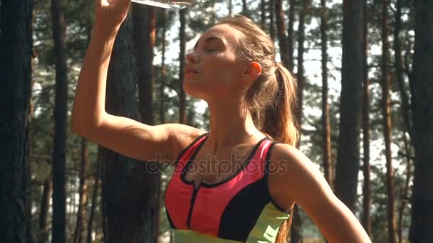 Сексуальная молодая атлетичная девушка стоит в лесу и заливает лицо водой — стоковое видео