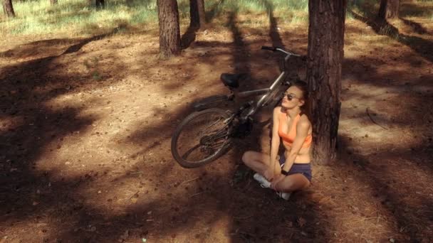 A gyönyörű fiatal hölgy ül egy fa alatt — Stock videók