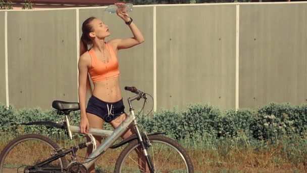 Mädchen mit Fahrrad übergießt sich mit Wasser aus Flaschen — Stockvideo