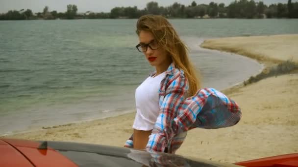 Junge schöne Mädchen mit roten Lippen und Brille stehen an einem Meeresufer — Stockvideo