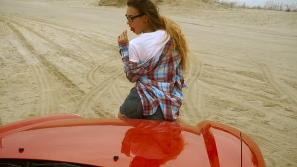 年轻热夫人坐在一辆红色汽车和舔棒棒糖 — 图库视频影像
