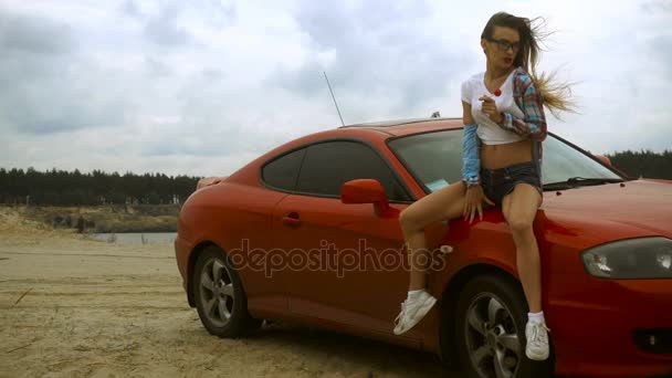 Sexy joven rubia se sienta en un coche rojo y lame una piruleta — Vídeos de Stock