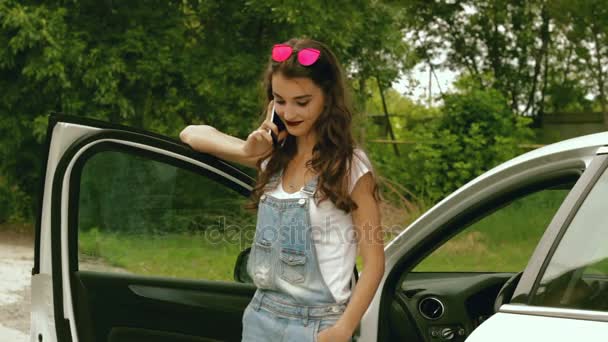 Señora de moda con gafas se para cerca de su coche y habla en un teléfono móvil — Vídeos de Stock