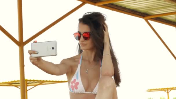 Fashionable brunette in glasses and a bathing suit makes a photo on your phone — Stock Video