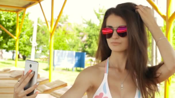 Schöne Mädchen mit Brille macht ein Foto auf dem Handy am Strand in einem Badeanzug — Stockvideo