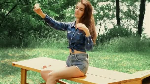 Beautiful brunette in a shirt and shorts sitting and makes a photo on your phone — Stock Video