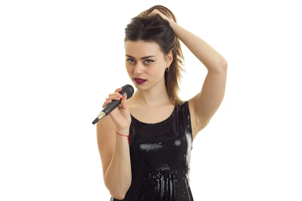 Incrível jovem morena mantém mão cabelo e canta em um microfone — Fotografia de Stock