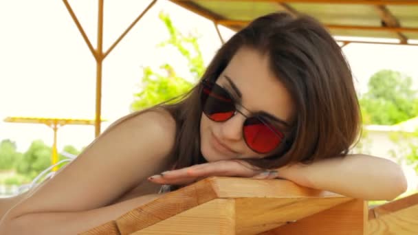ビーチで横になっているピンクの明るいメガネで美しい若い女性 — ストック動画