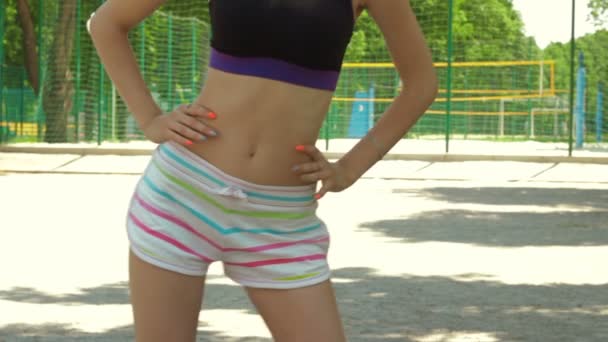 Молодая девушка с тонкой выпуклостью в шортах делает упражнения на улицах — стоковое видео