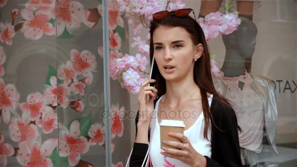コーヒーと電話で話してストア近くに若い女性が立っています。 — ストック動画
