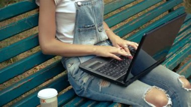 genç bir kadın bir bardak kahve ve bir dizüstü bilgisayar ile bir bankta oturur