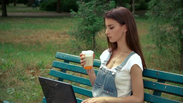 Beautiful brunette sits on the bench and watching in a laptop — Stock Video