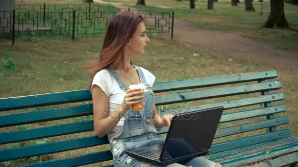 Uma jovem morena encantadora senta-se em um parque com um computador portátil — Vídeo de Stock