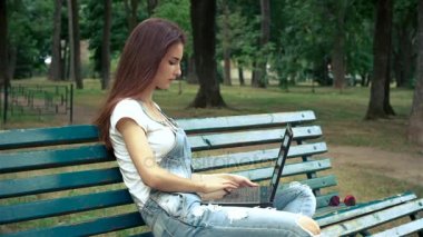 Park ve bir dizüstü bilgisayar üzerinde parmak bir bankta oturan genç esmer