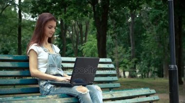 esmer kot pantolon ve parkta oturur bir dizüstü bilgisayarda yazdırır