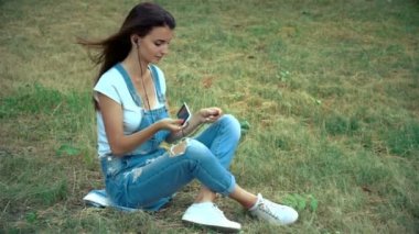 Pin-up kızı çimenlerin üzerinde oturur ve kulak içi kulaklıklar ekler