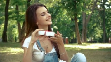mutlu kız parkta çim ve holding hediye kutusu üzerinde oturur