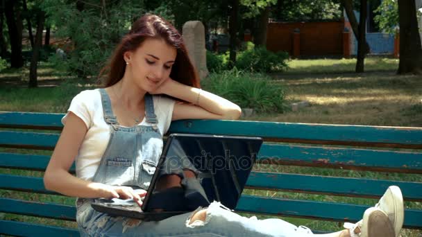 Menina atraente sentado em um banco com um laptop — Vídeo de Stock