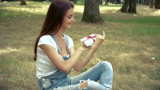 Joven feliz chica sostiene y trata regalo sentado fuera — Vídeos de Stock