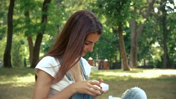 Morena linda se sienta en el verano en el parque y tiene un pequeño regalo — Vídeos de Stock