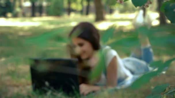 Schattige brunette met een laptop liggen op het groene gras — Stockvideo