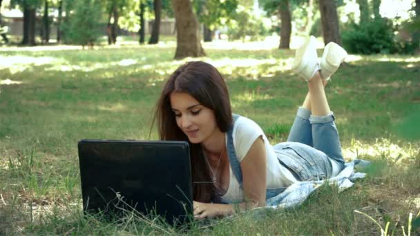 Giovane ragazza sdraiata sull'erba in estate e stampe su un computer portatile — Video Stock