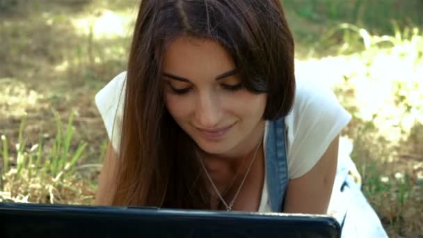 Schöne junge Mädchen auf dem Gras liegend auf Ihrem Laptop — Stockvideo