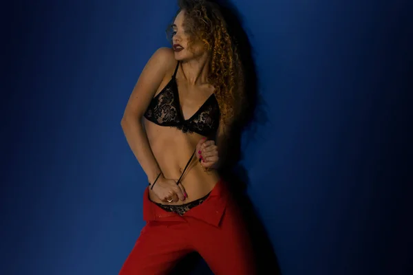 Sexuální mladá dáma s kudrnatými vlasy v podprsence a červené kalhoty — Stock fotografie