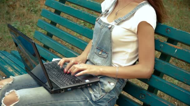 Flicka-kostym som sitter på en bänk och skriver på laptop — Stockvideo