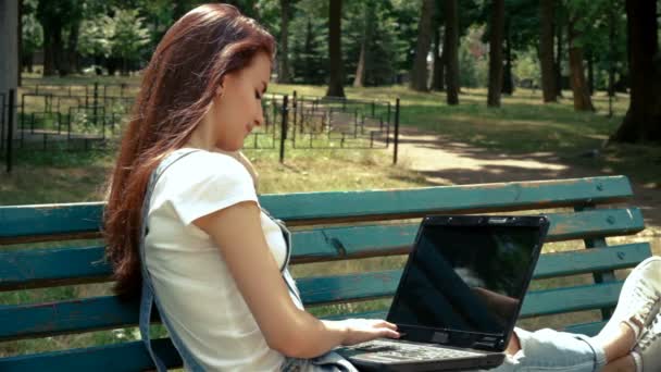 Очаровательная брюнетка сидит на скамейке с ноутбуком — стоковое видео