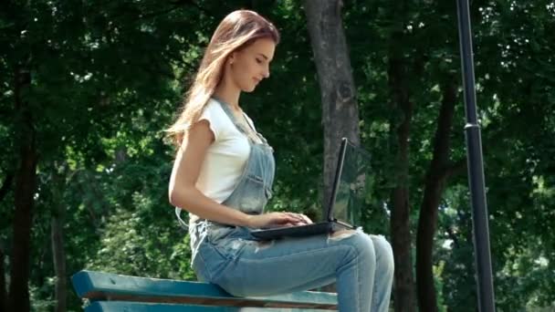 여름에는 거리에 앉고 있는 동안 노트북에 인쇄 하는 귀여운 여자 — 비디오