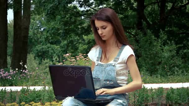 Девушка хранит отпечатки ноутбука рядом с клумбами на улице — стоковое видео