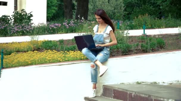 Красивая брюнетка в джинсовом платье держит ноутбук и отпечатки — стоковое видео