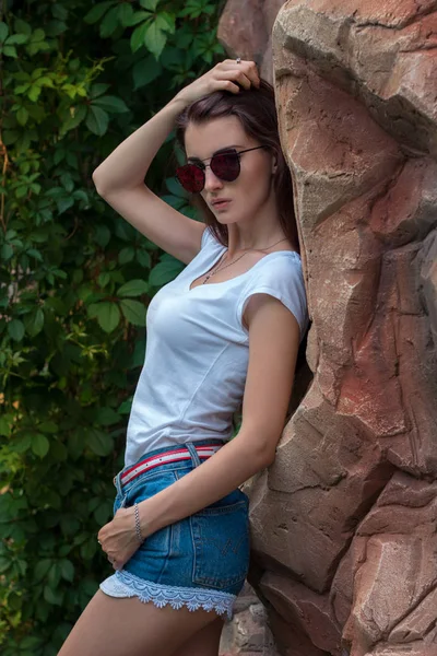 Sexy giovane signora in occhiali da sole in posa sulla macchina fotografica in piedi vicino alle pietre — Foto Stock