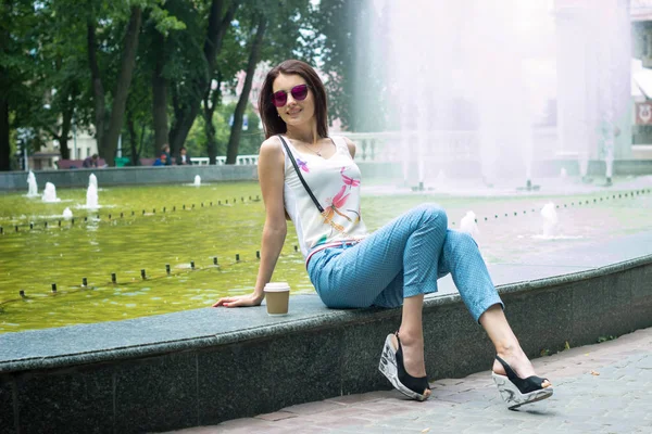 Bella ragazza in occhiali da sole seduto vicino alla fontana — Foto Stock