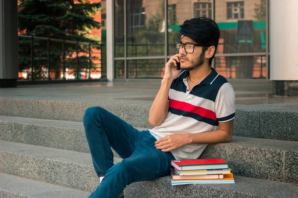 Jonge knappe kerel in glazen en boeken zittend op de trap — Stockfoto