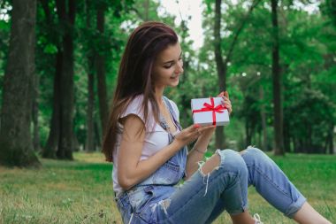 çim ve bir hediye tutan güzel nazik kız oturuyor