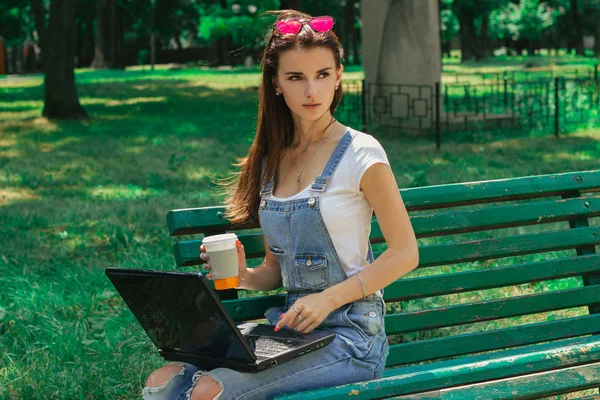 genç güzel kız düşünceli bir dizüstü bilgisayar tutan bankta oturur